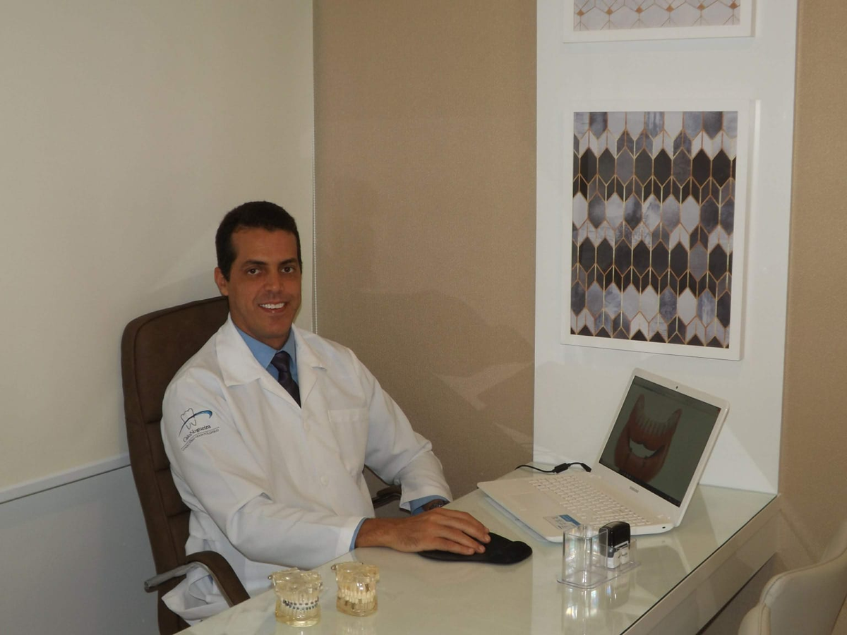 Dr. Caio Nogueira no consultório ao lado de notebook e modelos odontológicos